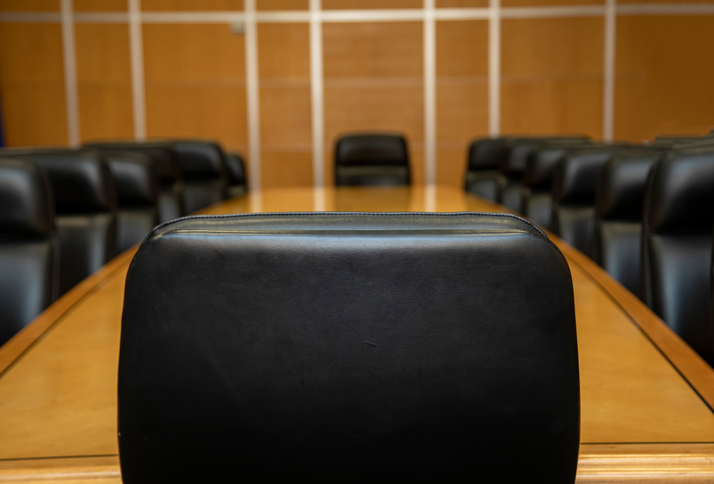 A clinical perspective view of an executive boardroom table, focusing on the vacant seat of authority to represent the structural redesign of the CMO role into a General Manager position.